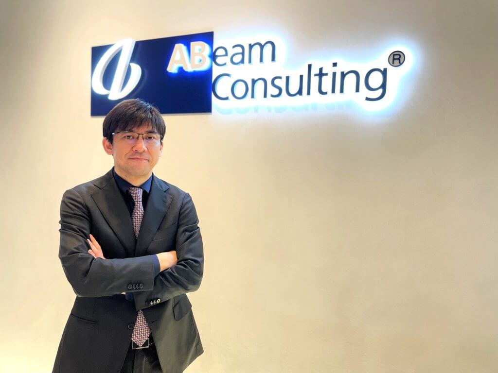 ABeam Consultingをバックに腕を組む男性